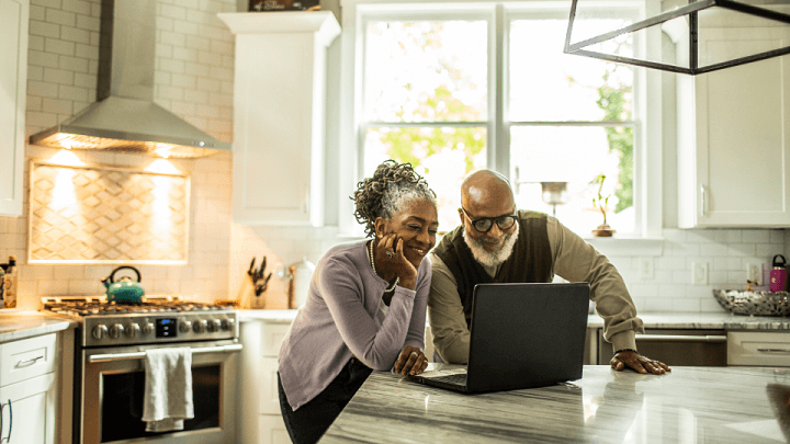 An elderly couple looking at a laptop together in their kitchen