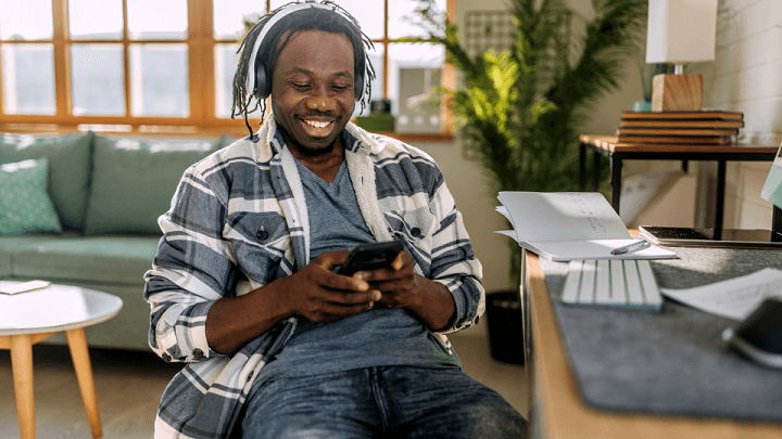 A man using his smartphone and wireless headphones at home